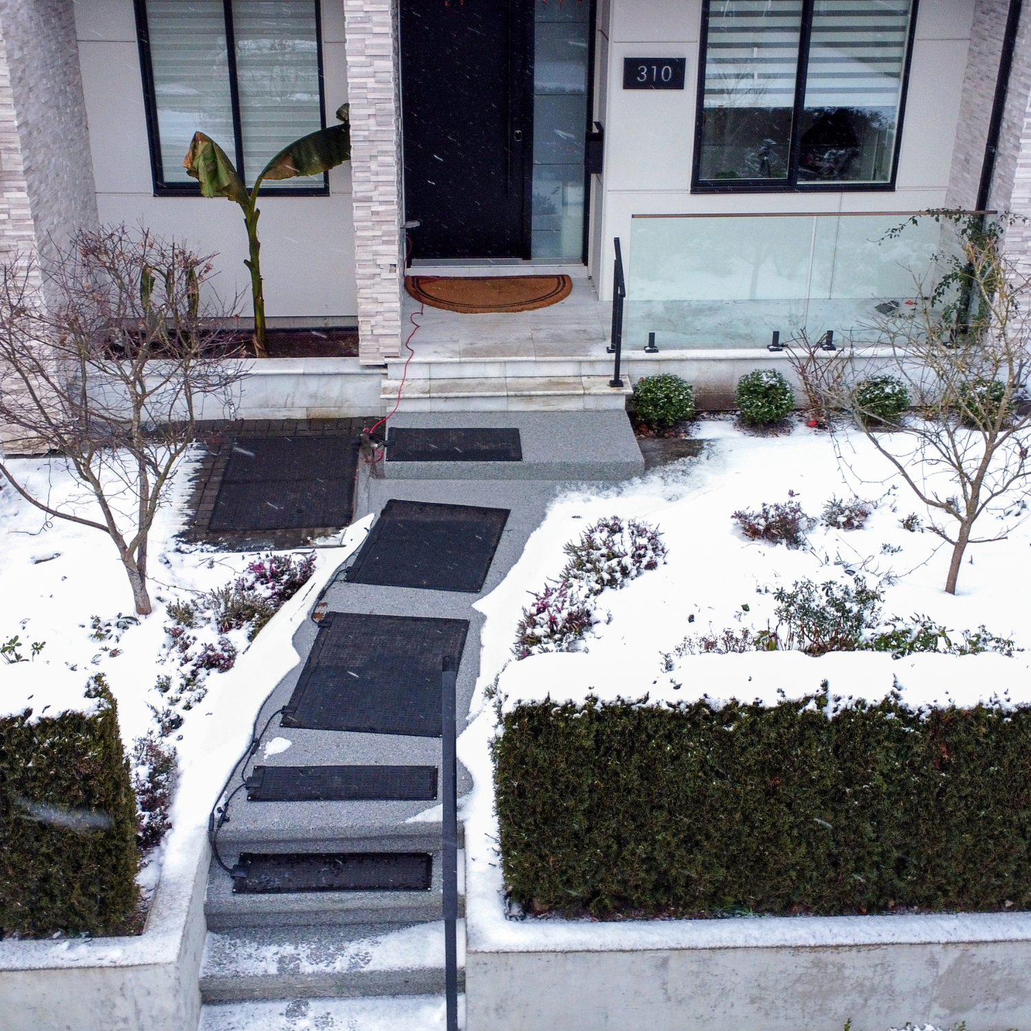 Front entrance of a house with snowmelt mats leading up to a door, snow on the ground